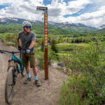 biker posing next to trail post