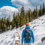 Tourist with backpack hiking on snowy trail in Rocky Mountains in Colorado