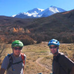 Two male bikers with a snowy mountain peak behind them