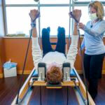 Woman instructing man laying on on pilates reformer