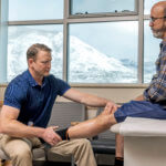 middle aged man getting knee examined in clinic room with mountains outside