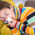 symptoms of seasonal allergies in colorado woman in a colorful striped sweater blowing her nose