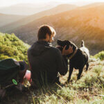 A man and a dog sitting on top of a mountain at sunset - Elevating Men’s Health at Every Age