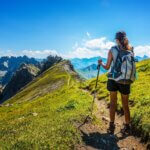 Hiker in boots and backpack holds walking stick as she pauses on dirt mountain pass guide to hiking injuries featured image