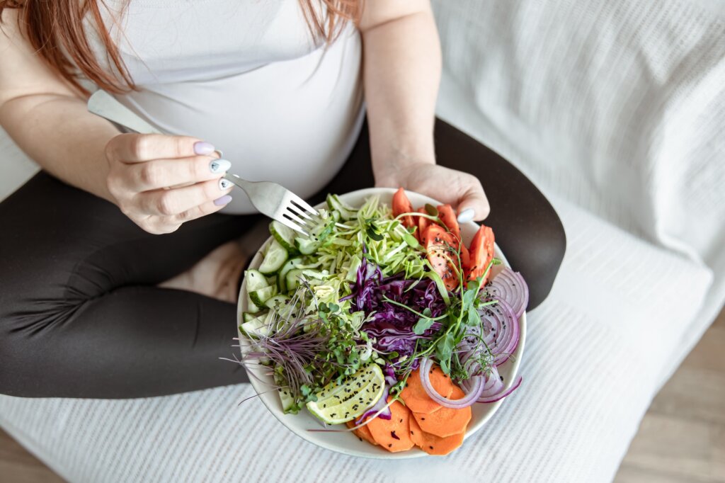 Close-up of a plate with a bright salad of fresh vegetables in the hands of a pregnant woman. caring for women’s hormones