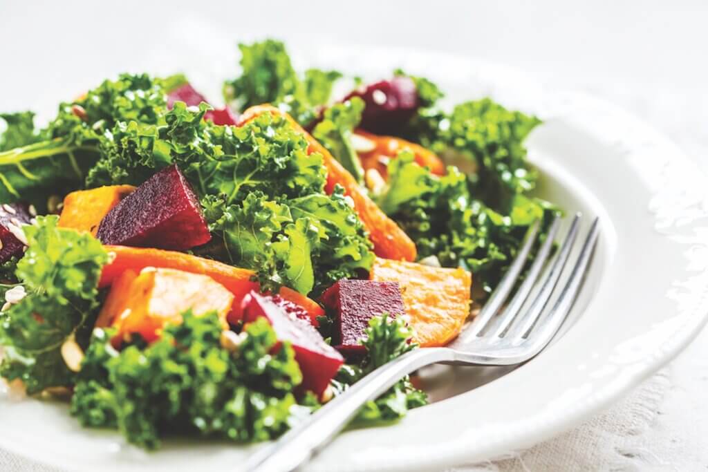 Kale salad with baked sweet potato, carrot and beet in a white plate.