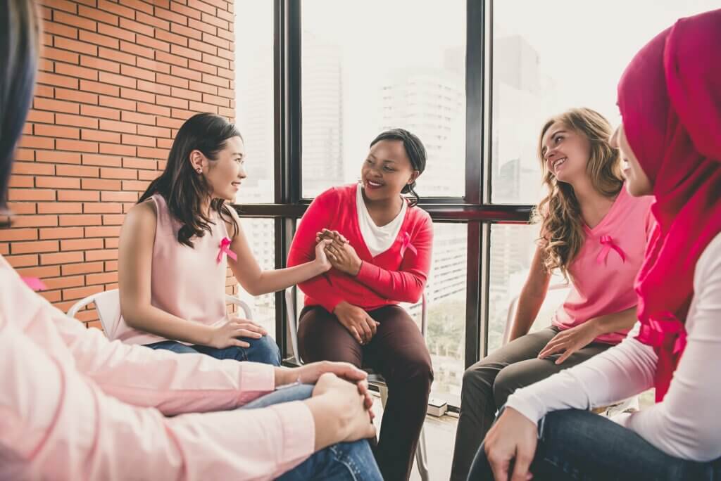 Multiethinic women wearing pink color clothes sitting in circle talking and meeting for breast cancer awareness campaign