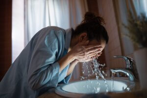 Woman washing her face in bathroom sink.