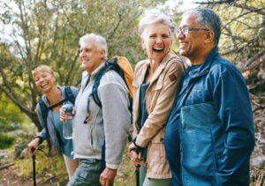 Nature, hiking and happy senior friends bonding, talking and laughing at comic joke in forest. Happiness, fun and group of elderly people trekking together for health, wellness and exercise in woods mental health while aging