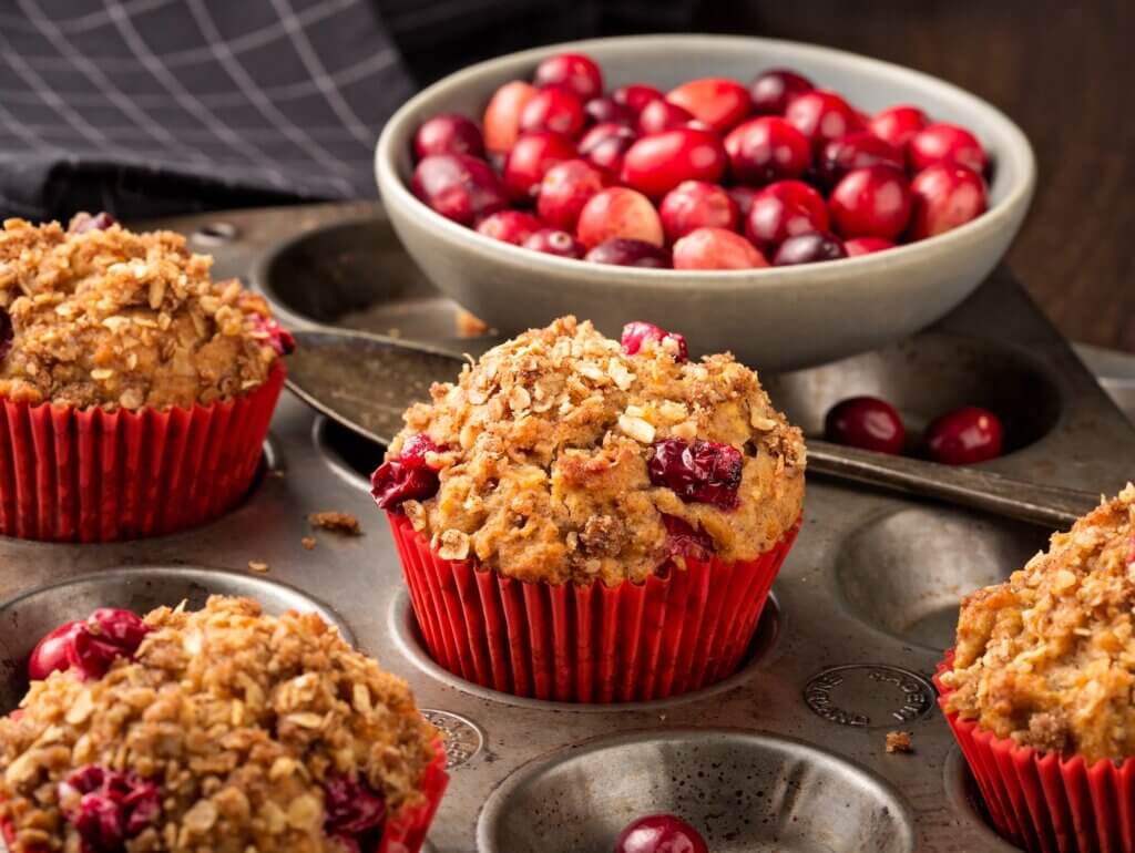 Freshly baked cranberry muffins with oatmeal crumble topping in a rustic muffin tin.