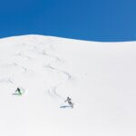 Man and woman skiing down mountain leaving tracks behind