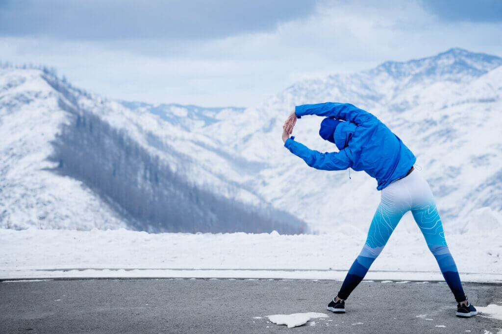 Athlete at the top of the mountain doing stretching. Training in the winter.