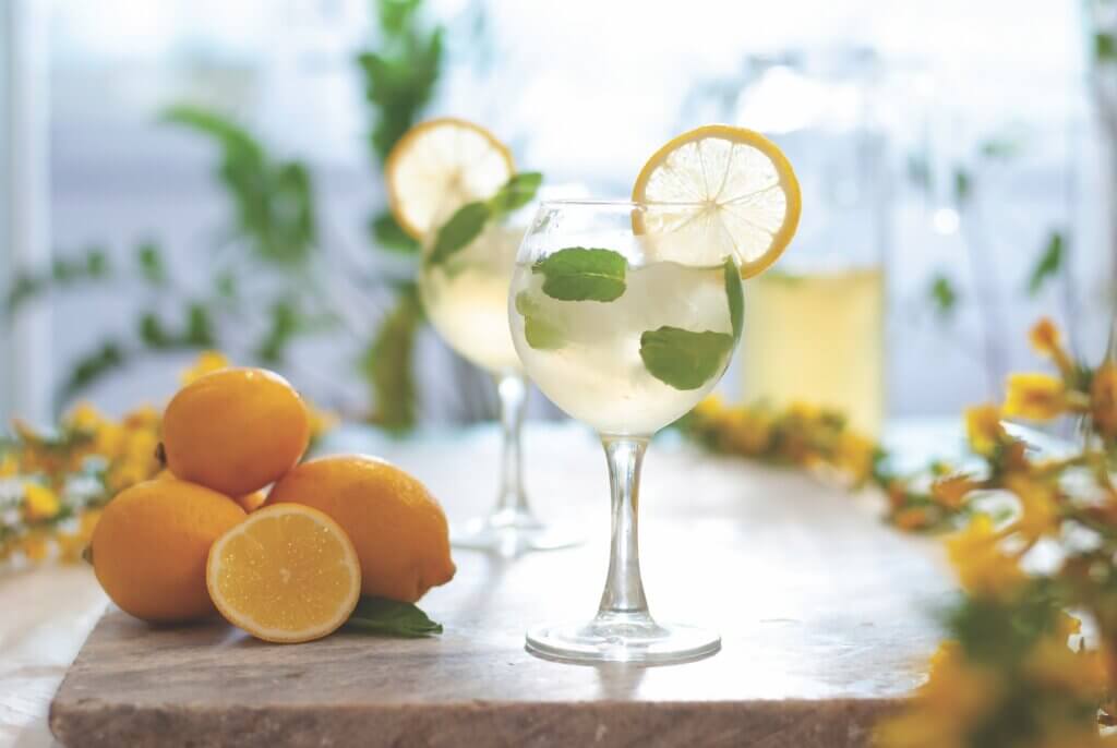 Citrus iced lemonade in pitcher and glasses with lemon slice and mint leaves decoration and on marble table on natural background. Fresh summer drink beautiful picture